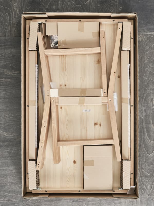 An IKEA flatpack with the top removed revealing a pine chair waiting to be assembled.
