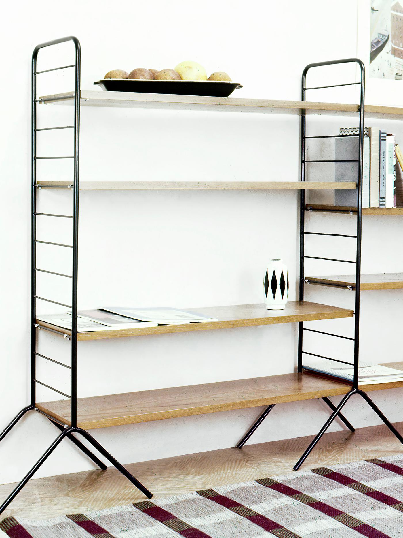An IKEA HANSA shelving unit from 1957 consisting of dark metal frames and legs and wooden shelves.