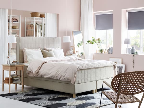 An IKEA HOMMELVIK beige divan bed, with fabric headboard, boldly placed in the middle of a pink bedroom.
