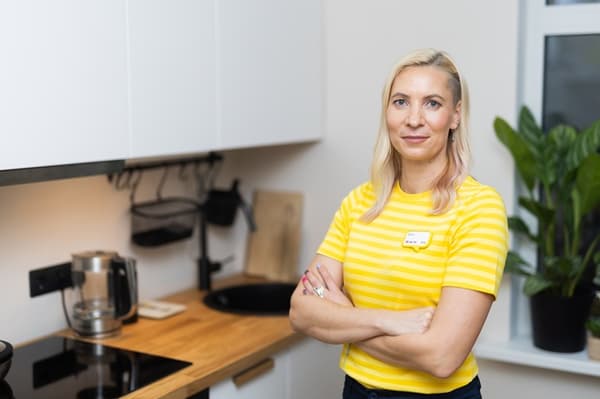 An IKEA interior designer in a yellow uniform shirt stands in a kitchen with white fronts and a wooden worktop.