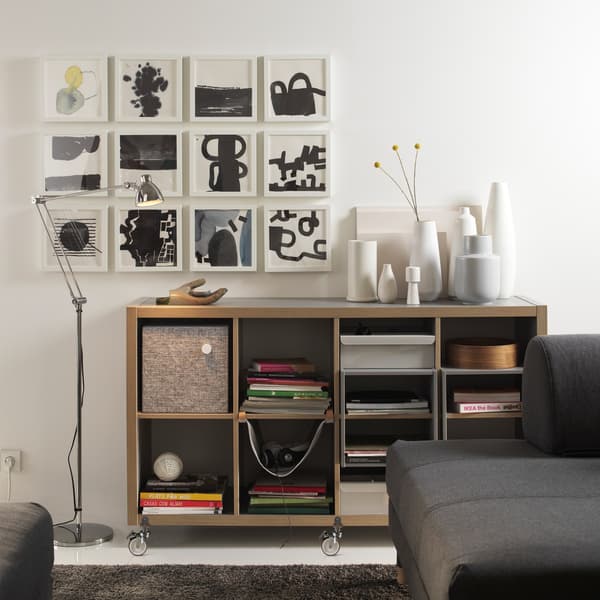 An IKEA KALLAX grey/wood shelving unit with lots of vases on top and lots of artwork on the wall.