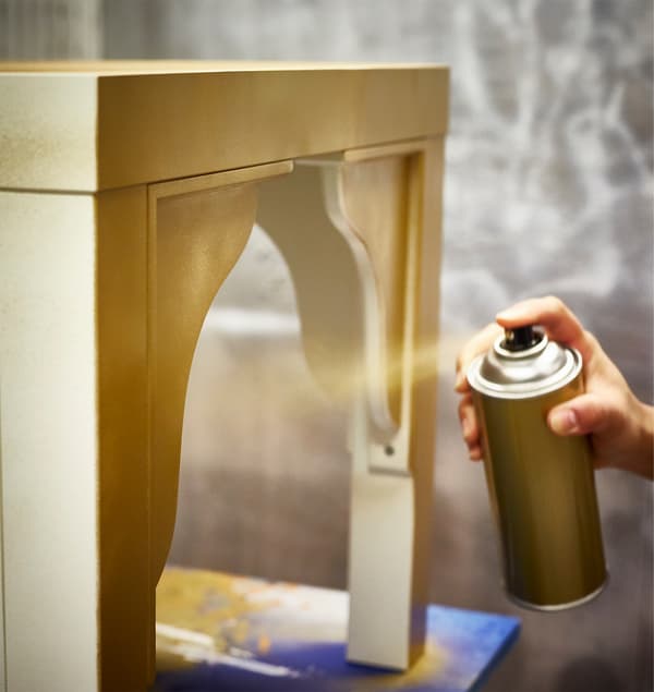 An IKEA LACK table is being spray-painted gold.