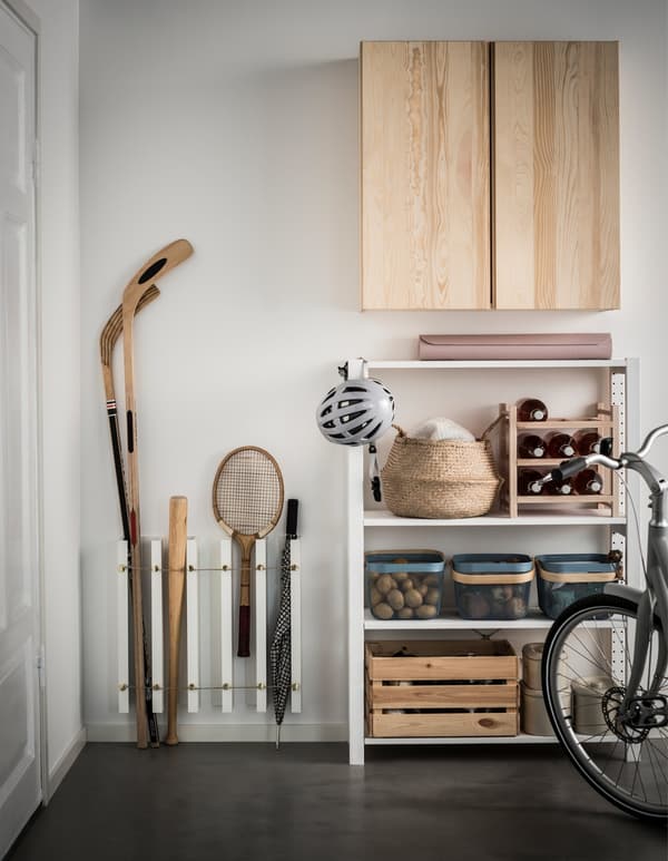 An IKEA MOSSLANDA hack stores sports equipment vertically in a garage with other storage solutions, like a cabinet.