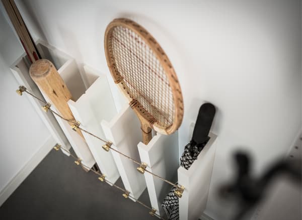 An IKEA MOSSLANDA hack using picture ledges secured vertically with tennis rackets, hockey sticks, baseball bats and umbrellas stored upright