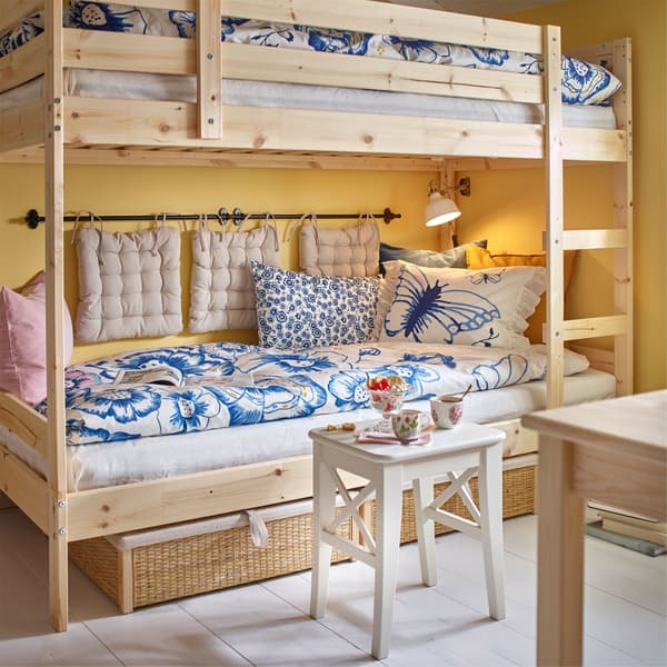 An IKEA MYDAL bunk bed, with the lower bunk used as a daybed, with extra cushions hung on the wall and blue floral bed linen.