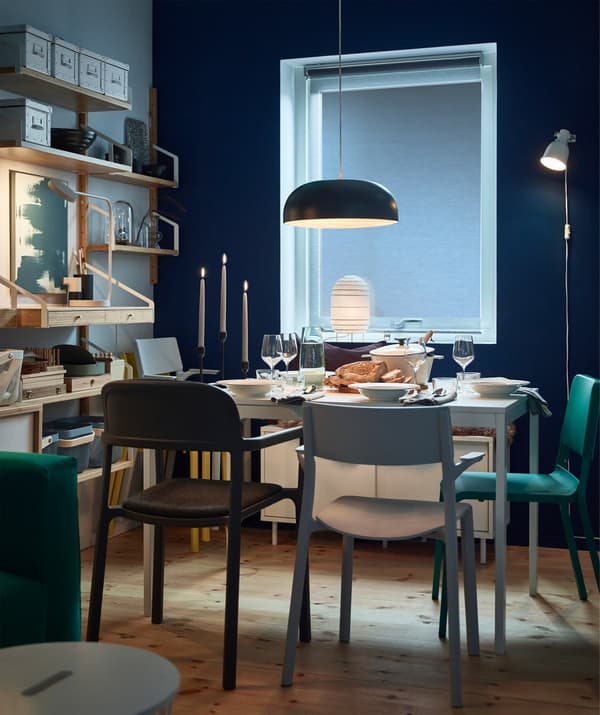 An IKEA NYMÅNE black steel pendant lamp suspended above a dining table in a darkened blue room.