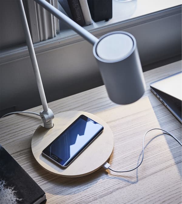 An IKEA RIGGAD work lamp and wireless charger with a mobile phone on charge.