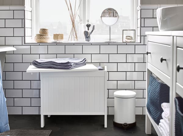 An IKEA SILVERÅN white storage bench with a partially opened lid, with a folded towel on top.