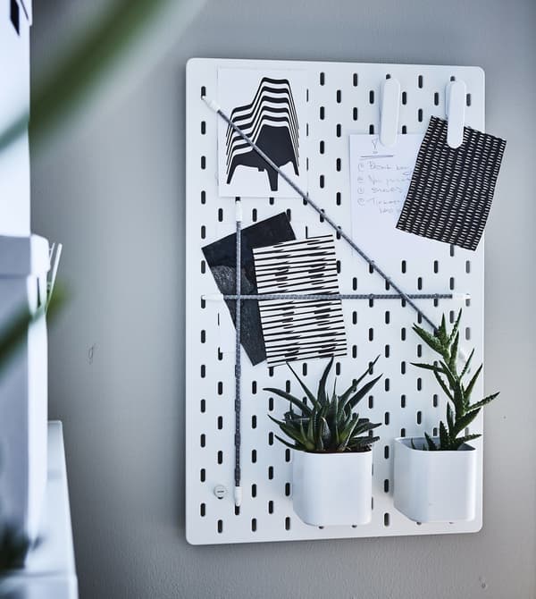 An IKEA SKÅDIS pegboard decorated with plants and notes.