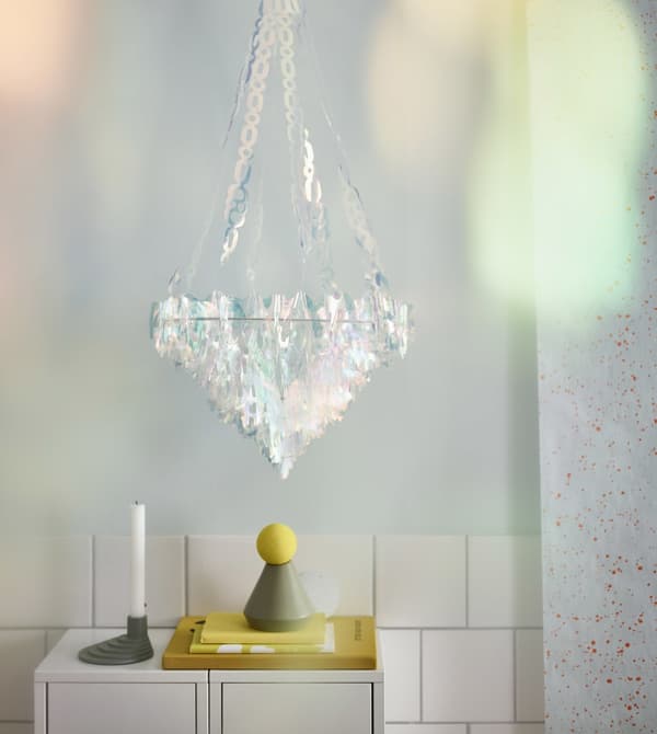 An IKEA VINTER 2017 hanging chandelier made of plastic, iridescent pieces that look like crystals glows in a room.