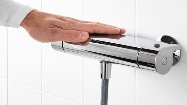 An image of a hand put on a shower mixer on a white tile wall.