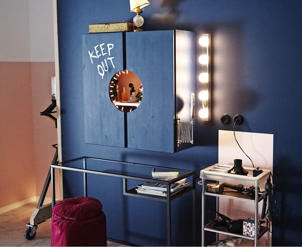 An image of a vanity station that consists of a cabinet, a small table and a place for the bathroom cart. The walls and cabinet are painted dark blue.