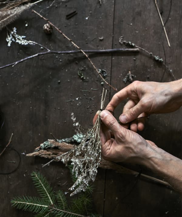 An image of hands tying a sprig of foliage with black sewing thread.