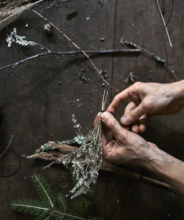 An image of hands tying a sprig of foliage with black sewing thread.