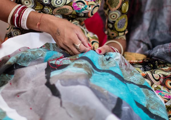 An Indian artisan embroidering a cushion cover with a modern, irregular print in turquoise, grey and black.