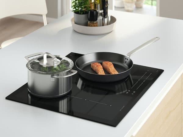 An induction black hob with a pot and pan on top.