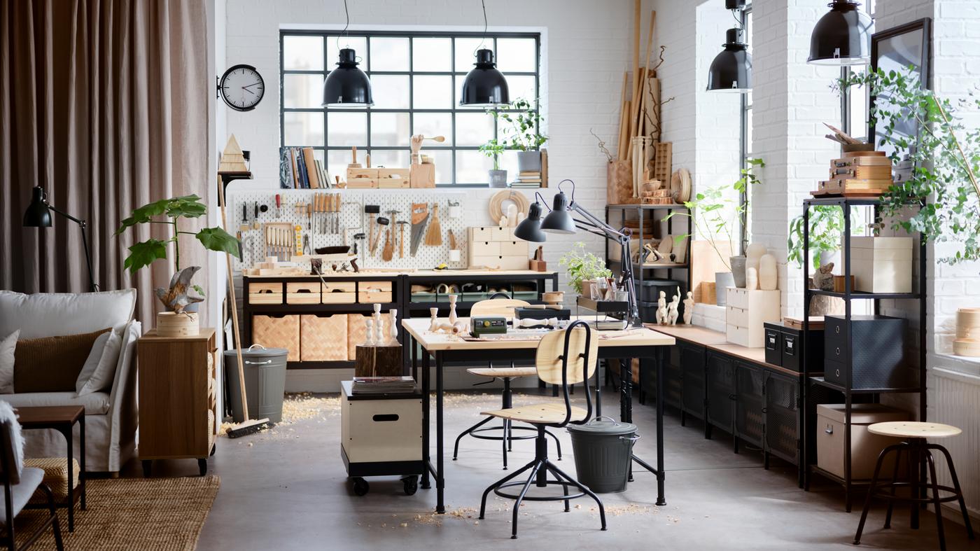An industrial-style studio at home with high ceilings, furniture made from wood and black metal, and big windows.