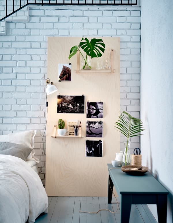 An inspiration board made of plywood leaning against a white brick wall in the bedroom.