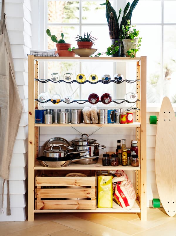 An IVAR unit stands by a window, organised as a small pantry with pots, dry goods, canned food, and bottles on racks.