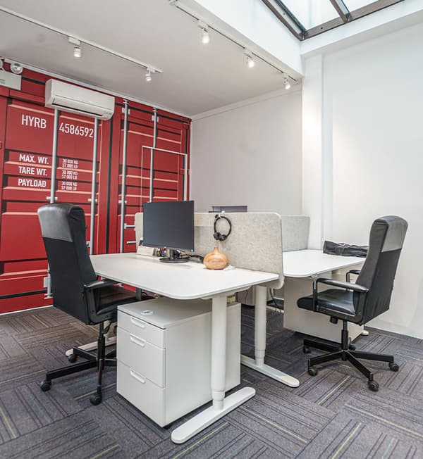 An office area showing white tables and drawers partition with grey partition walls. 