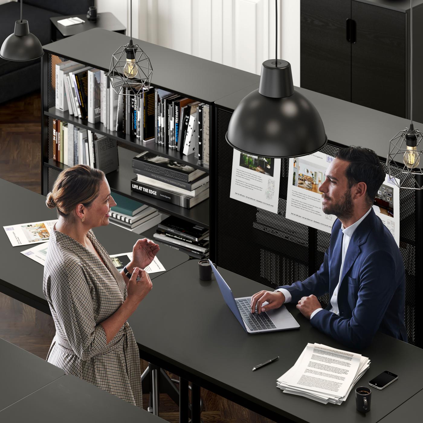 An office setting where a woman talks to a man in a suit who sits with his laptop by a TOMMARYD table.