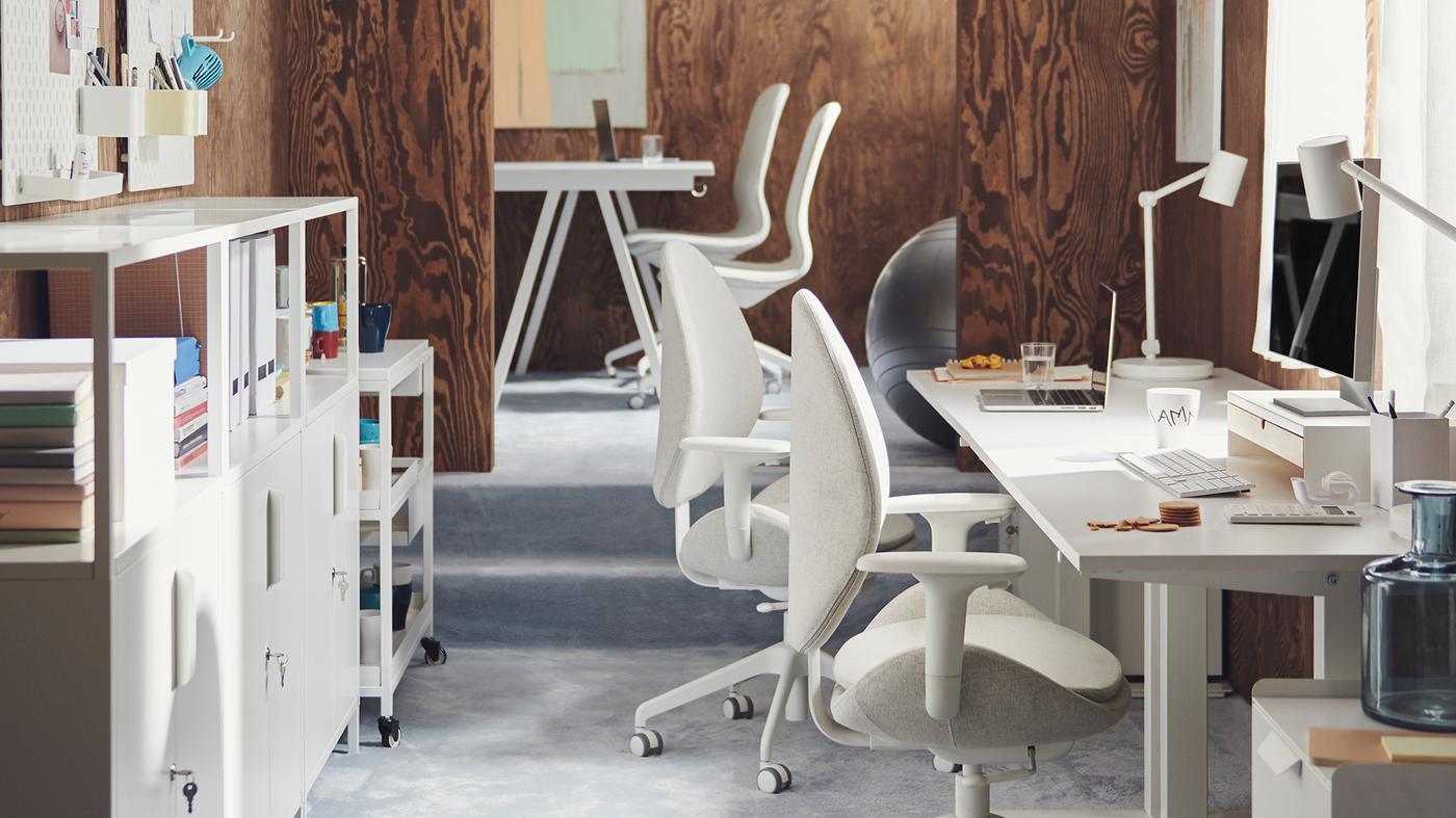 An office space featuring two white tables and swivel chairs with office equipment around the room and a storage cabinet at the back.