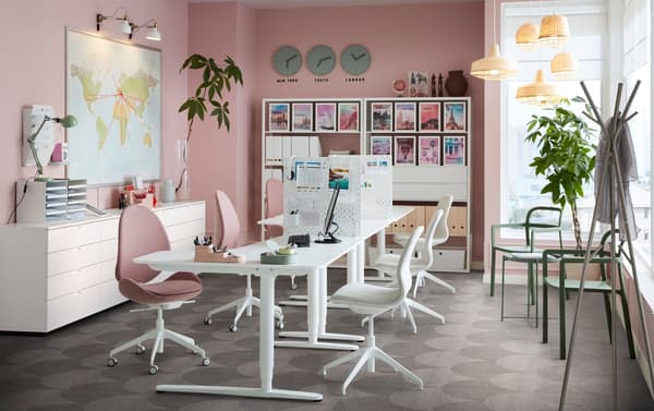 An office space with pink walls and white BEKANT sit-stand work desks, with HATTEFJÄLL swivel chairs.