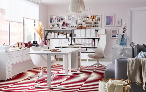 An office with white chairs, a white sit/stand desk, and a red and white striped rug