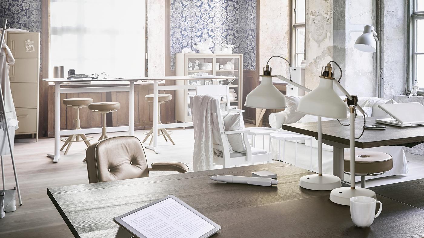 An office workspace with various desks and seating, with table lamps, a floor lamp, plus open and closed storage units.