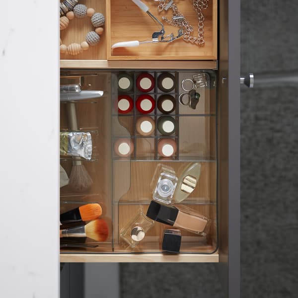 An open bathroom drawer holding an organiser in transparent plastic with make-up, and bamboo boxes with accessories.