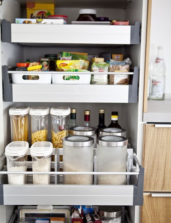 An open high cabinet reveals a pantry of dry goods stored in jars and bins in drawers.
