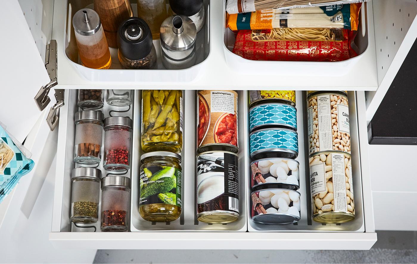 An open IKEA MAXIMERA white kitchen pantry drawer displaying organized cans, spices and oils.