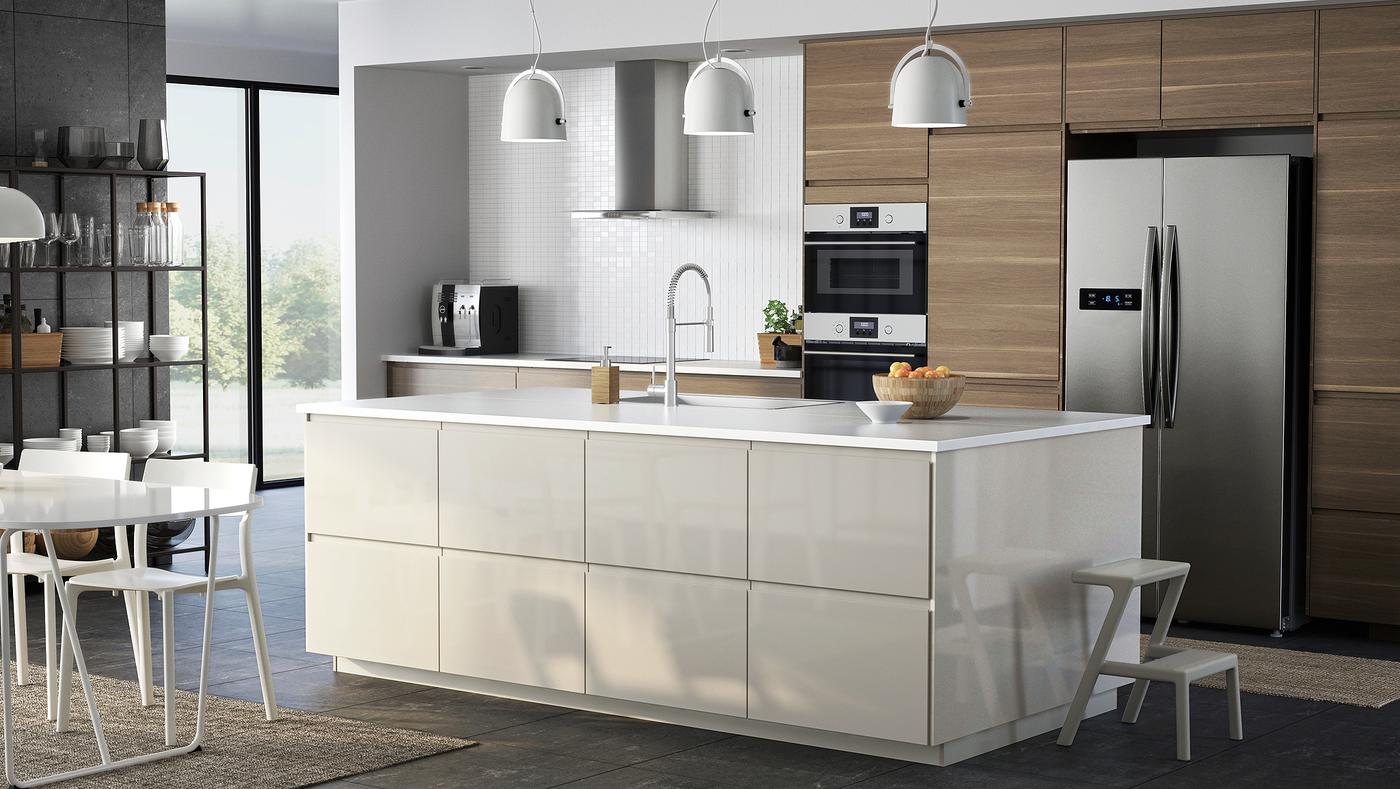 An open kitchen with a kitchen island and a mix of high-gloss light-beige and walnut-effect fronts, a table and chairs.