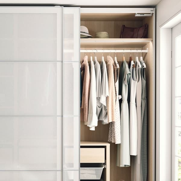 An open PAX wardrobe with white sliding doors has a white stained oak effect interior with clothes, baskets and drawers.
