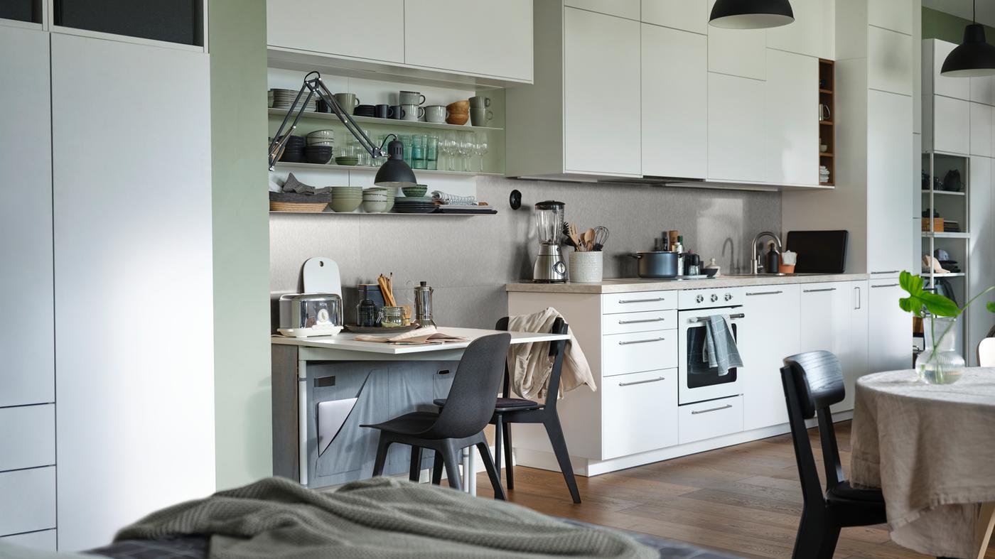 An open plan apartment with a KALLHÄLL gateleg table with storage and a white METOD kitchen with floor to ceiling cabinets.