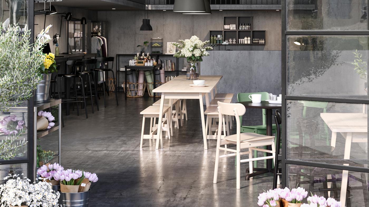 An open plan cafe, shop and co-working space framed by open glass doors. Flowers are on the table and by the doors.