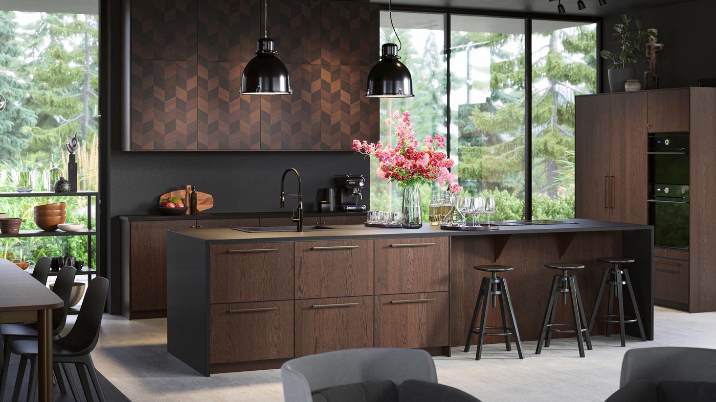 An open plan kitchen with floor to ceiling windows, SINARP drawers and HASSLARP doors, black pendant lamps and bar stools.