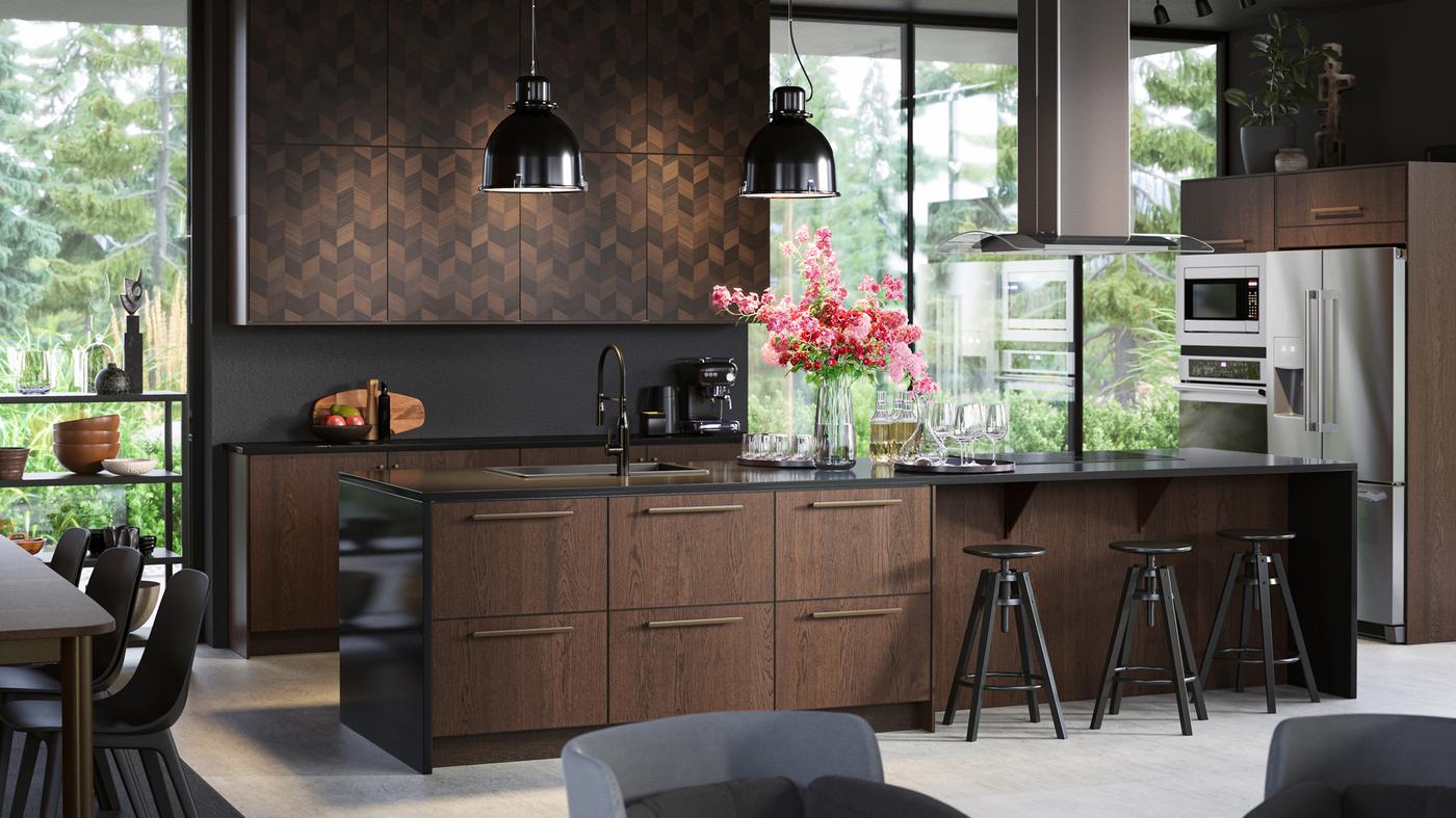 An open plan kitchen with floor to ceiling windows, SINARP drawers and HASSLARP doors, black pendant lamps and bar stools.