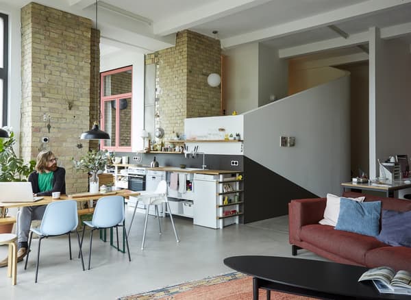 An open-plan living room, kitchen, and dining space in a converted loft with brick walls.