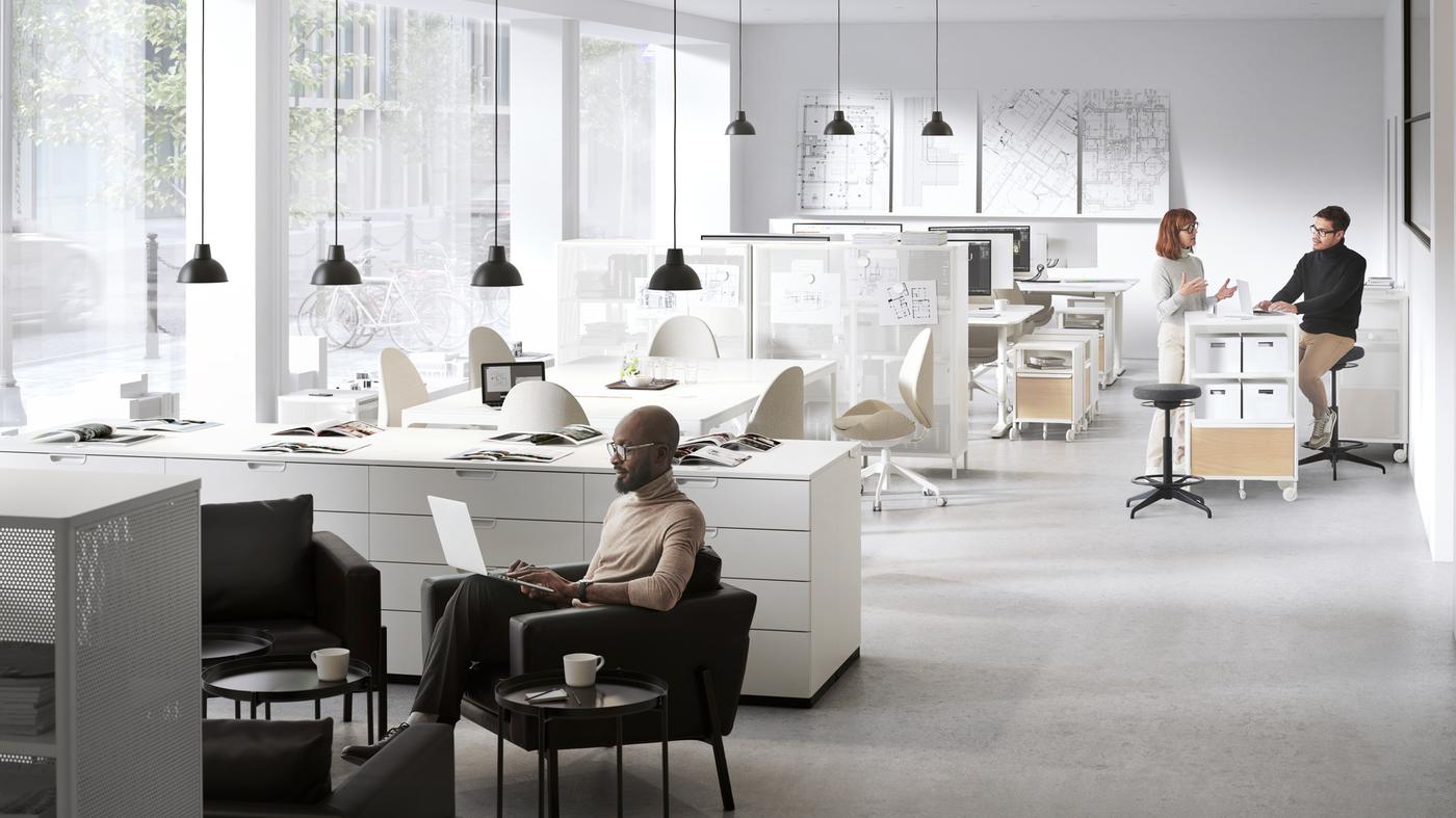 An open plan office with two breakout zones. A man works in a KOARP armchair and two people chat over a shelving unit.