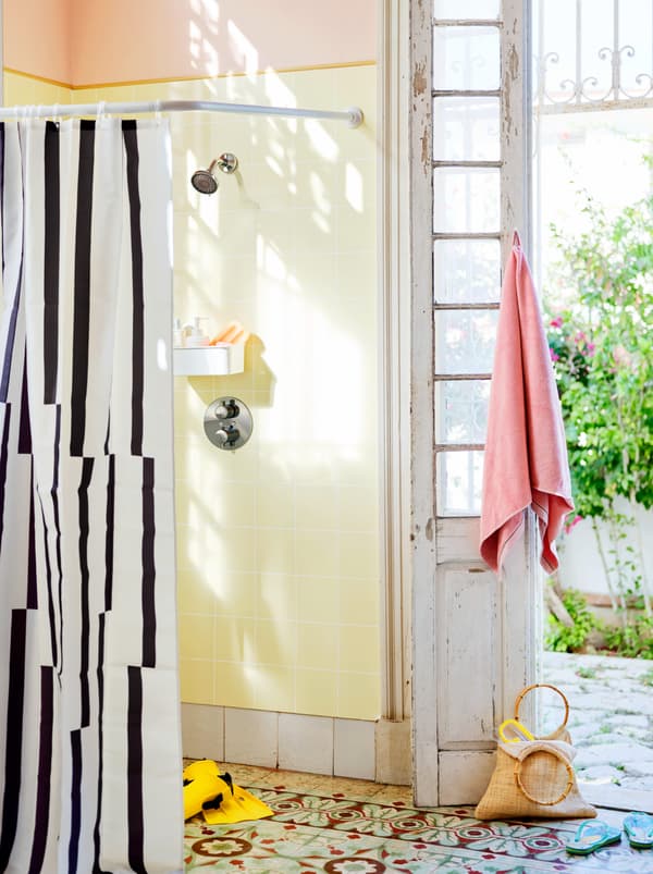An open shower with a black and white shower curtain, next to an open white-washed wooden door.