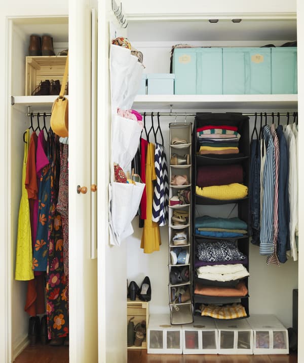 An opened closet door showing a black hanging clothes organiser with folded clothes inside to maximise storage space.