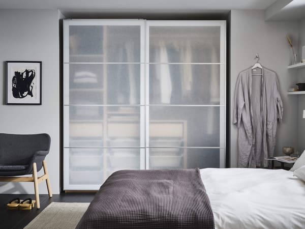 An organised bedroom with a wardrobe behind sliding doors and a robe to the side of it.