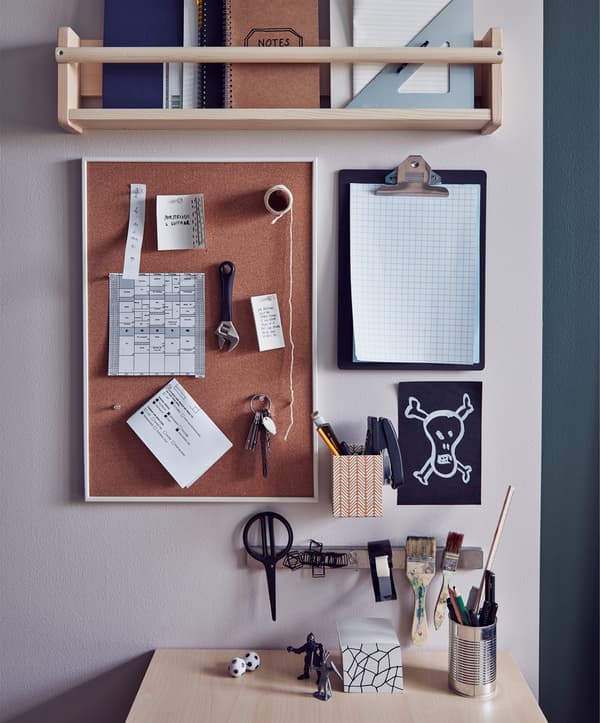 An organised wall next to a desk with a shelving unit, a clipboard and a noticeboard
