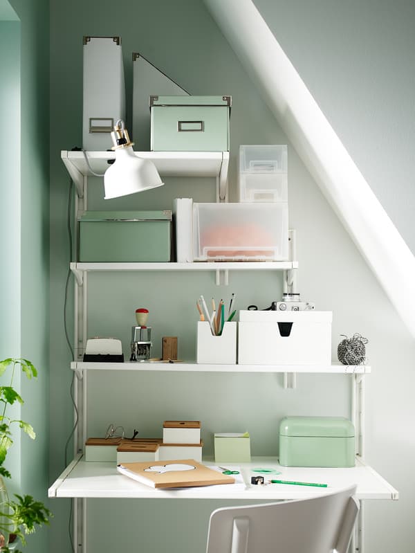 An organised work station under a sloped ceiling, made using IKEA wall storage with shelves of different widths.
