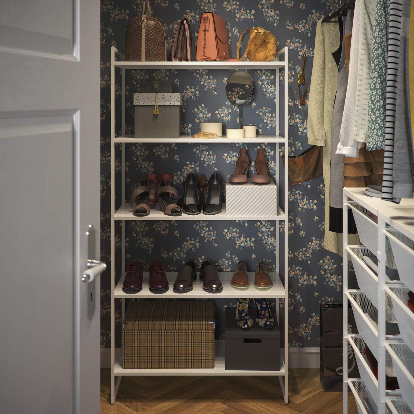 An organized corner of a room with a JONAXEL white shelving unit holding various pairs of shoes, bags, and a box. The room is decorated with dark floral wallpaper.