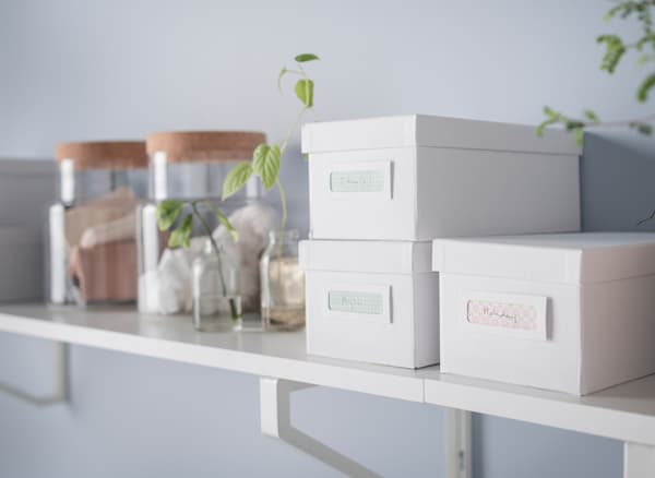 An organized desk without drawers in white and light wood with a shelf above it and lots of boxes, jars and vases for storage.