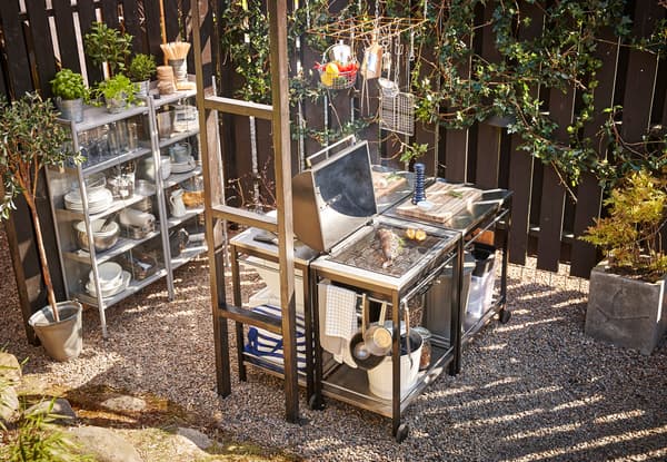 An outdoor kitchen made with 3 serving carts, a grill and a cabinet.