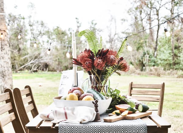 An outdoor table set with flowers and fresh produce.