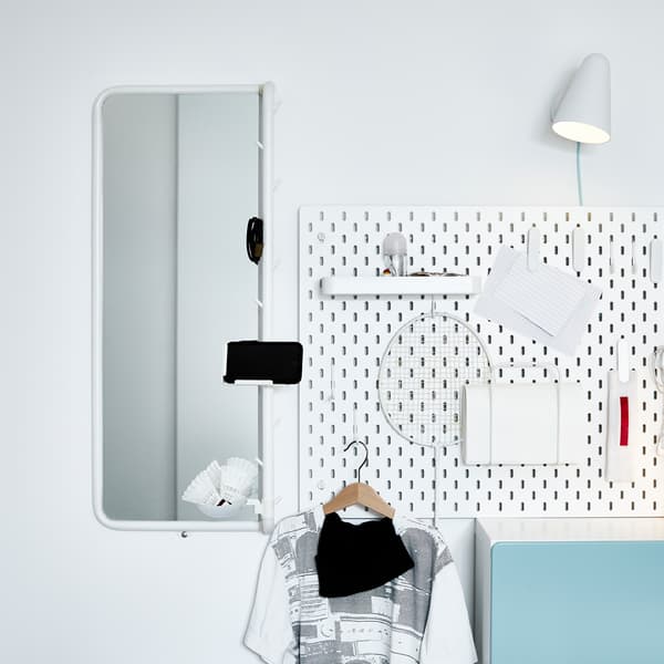 An outfit corner with a white pegboard, a white wall lamp and a white mirror with a phone holder.